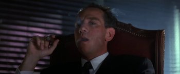 Movie still from “Point of No Return” (1993), directed by John Badham – A man in a suit and tie smoking a cigarette; Close Up shot, Low angle