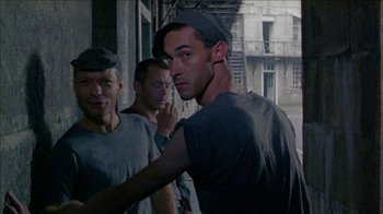 Movie still from “Poison” (1991), directed by Todd Haynes – A group of men standing next to each other on a street; Medium shot, Over the shoulder angle
