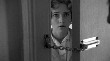 Movie still from “Poison” (1991), directed by Todd Haynes – A young woman in a white dress shirt is looking through a door; Close Up shot, Low angle