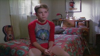Movie still from “Poison” (1991), directed by Todd Haynes – A young boy sitting on a bed in a room; Medium shot, High angle