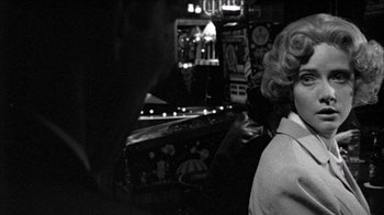 Movie still from “Poison” (1991), directed by Todd Haynes – A black and white photo of a woman standing in front of a pinball machine; Close Up shot, Over the shoulder angle