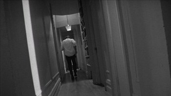 Movie still from “Poison” (1991), directed by Todd Haynes – A man walking down a long hallway in a house; Wide shot, High angle