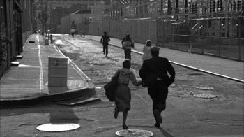 Movie still from “Poison” (1991), directed by Todd Haynes – A black and white photo of people walking down a street; Wide shot, High angle