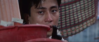 Movie still from “Police Story” (1985), directed by Jackie Chan – A young man is sitting down and holding a cell phone to his mouth; Close Up shot, High angle