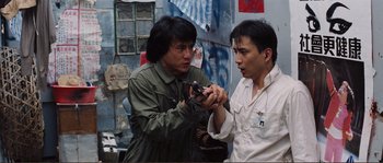 Movie still from “Police Story” (1985), directed by Jackie Chan – A man holding a cell phone next to another man; Medium shot, High angle
