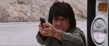 Movie still from “Police Story” (1985), directed by Jackie Chan – A man holding a gun in his hands; Close Up shot, Low angle