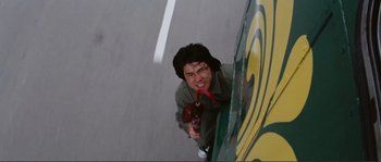 Movie still from “Police Story” (1985), directed by Jackie Chan – A man holding a red object in his mouth; Medium shot, Overhead angle