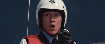 Movie still from “Police Story” (1985), directed by Jackie Chan – A police officer wearing a white helmet and black gloves; Close Up shot, Low angle