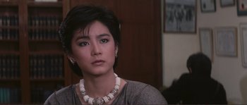 Movie still from “Police Story” (1985), directed by Jackie Chan – A person wearing a necklace and looking at the camera; Close Up shot, High angle