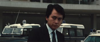 Movie still from “Police Story” (1985), directed by Jackie Chan – A person wearing a suit and tie; Close Up shot, Low angle