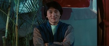 Movie still from “Police Story” (1985), directed by Jackie Chan – A man with his arms crossed in front of a plant; Medium shot, Low angle