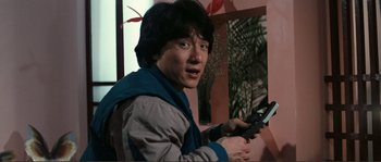 Movie still from “Police Story” (1985), directed by Jackie Chan – A man holding a cell phone in his hand; Medium shot, Low angle