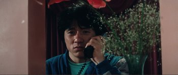Movie still from “Police Story” (1985), directed by Jackie Chan – A man talking on a phone next to some flowers; Close Up shot, Low angle