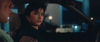 Movie still from “Police Story” (1985), directed by Jackie Chan – A woman sitting in the driver's seat of a car at night; Close Up shot, Over the shoulder angle