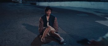 Movie still from “Police Story” (1985), directed by Jackie Chan – A person sitting on the ground on a street; Wide shot, High angle