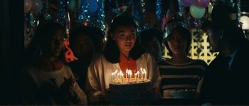 Movie still from “Police Story” (1985), directed by Jackie Chan – A girl holding a birthday cake with lit candles on it; Medium shot, High angle