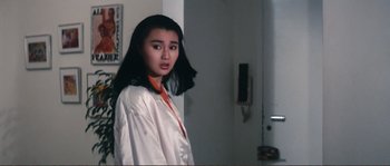 Movie still from “Police Story” (1985), directed by Jackie Chan – A young woman in a white shirt is standing in a room; Medium shot, Over the shoulder angle