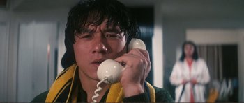 Movie still from “Police Story” (1985), directed by Jackie Chan – A man holding a phone to his ear while wearing a towel around his neck; Close Up shot, Low angle