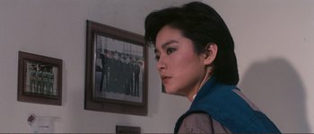 Movie still from “Police Story” (1985), directed by Jackie Chan – A woman standing in front of a picture of a group of people; Close Up shot, Over the shoulder angle