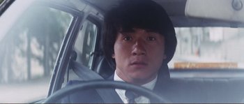 Movie still from “Police Story” (1985), directed by Jackie Chan – A man in a suit and tie sitting in the driver's seat of a car; Close Up shot, Low angle