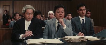 Movie still from “Police Story” (1985), directed by Jackie Chan – A group of people sitting at a table in front of papers; Medium shot, High angle
