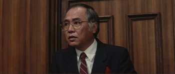 Movie still from “Police Story” (1985), directed by Jackie Chan – An older man wearing a suit and tie; Close Up shot, Low angle