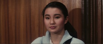 Movie still from “Police Story” (1985), directed by Jackie Chan – A young woman with long black hair wearing a white jacket; Close Up shot, High angle