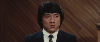 Movie still from “Police Story” (1985), directed by Jackie Chan – A man in a suit and tie wearing a wig; Close Up shot, Low angle