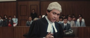 Movie still from “Police Story” (1985), directed by Jackie Chan – A man in a court room wearing a judge's wig; Medium shot, Low angle