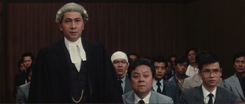 Movie still from “Police Story” (1985), directed by Jackie Chan – A group of men in suits and ties standing in a courtroom; Medium shot, Low angle