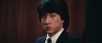 Movie still from “Police Story” (1985), directed by Jackie Chan – A person wearing a suit and tie; Close Up shot, Low angle