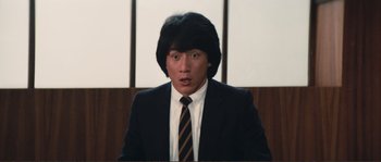 Movie still from “Police Story” (1985), directed by Jackie Chan – A man in a black suit and a black tie; Close Up shot, Low angle