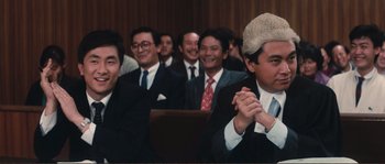Movie still from “Police Story” (1985), directed by Jackie Chan – A group of men in suits and ties sitting in a room; Medium shot, Low angle