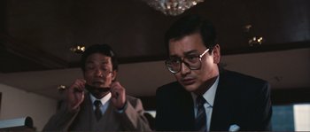 Movie still from “Police Story” (1985), directed by Jackie Chan – A man in a suit and tie next to another man in a suit and tie; Close Up shot, Low angle