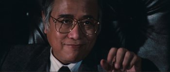 Movie still from “Police Story” (1985), directed by Jackie Chan – An older man wearing glasses and a suit and tie; Close Up shot, Low angle