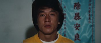 Movie still from “Police Story” (1985), directed by Jackie Chan – A man with a yellow shirt is looking at the camera; Close Up shot, Low angle
