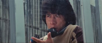 Movie still from “Police Story” (1985), directed by Jackie Chan – A man holding a cell phone up to his face; Close Up shot, Low angle