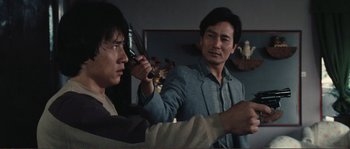 Movie still from “Police Story” (1985), directed by Jackie Chan – Two asian men in a living room holding guns; Close Up shot, Over the shoulder angle