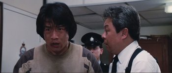 Movie still from “Police Story” (1985), directed by Jackie Chan – A man in a brown shirt and a man in a black tie; Close Up shot, Low angle
