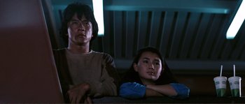 Movie still from “Police Story” (1985), directed by Jackie Chan – A man and a woman sitting next to each other on a couch; Medium shot, Low angle