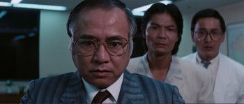 Movie still from “Police Story” (1985), directed by Jackie Chan – A man and a woman wearing glasses in a room; Close Up shot, Over the shoulder angle