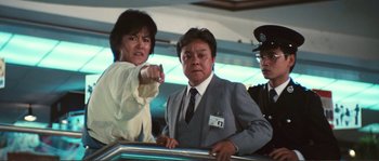 Movie still from “Police Story” (1985), directed by Jackie Chan – A man and a woman standing next to each other in front of another man; Medium shot, Low angle