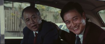 Movie still from “Police Story 2” (1988), directed by Jackie Chan – Two men in suits in the back seat of a car; Close Up shot, Over the shoulder angle