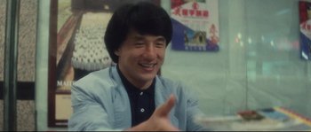 Movie still from “Police Story 2” (1988), directed by Jackie Chan – A man in a blue shirt is smiling and holding his hand out; Close Up shot, Over the shoulder angle