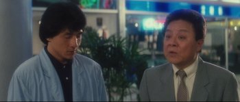 Movie still from “Police Story 2” (1988), directed by Jackie Chan – Two people standing next to each other in front of a plant; Medium shot, Over the shoulder angle