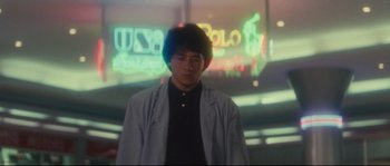 Movie still from “Police Story 2” (1988), directed by Jackie Chan – A man standing in front of a neon sign at night; Medium shot, Low angle