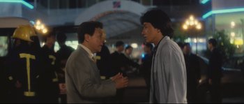 Movie still from “Police Story 2” (1988), directed by Jackie Chan – Two men talking to each other in a crowd of onlookers; Medium shot, Over the shoulder angle