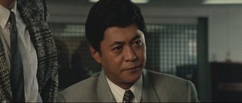 Movie still from “Police Story 2” (1988), directed by Jackie Chan – A person wearing a suit and tie; Close Up shot, Low angle