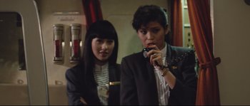 Movie still from “Police Story 2” (1988), directed by Jackie Chan – Two women in suits are standing next to each other; Medium shot, Over the shoulder angle