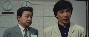 Movie still from “Police Story 2” (1988), directed by Jackie Chan – Two men in suits and ties standing next to each other in front of a wall; Close Up shot, Low angle
